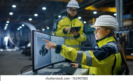 Inside the Heavy Industry, Factory Female Industrial Engineer Works on Personal Computer She Designs 3D Engine Model, Her Male Colleague Talks with Her and Uses Tablet Computer. Low Angle Shot. - Shutterstock ID 761907082