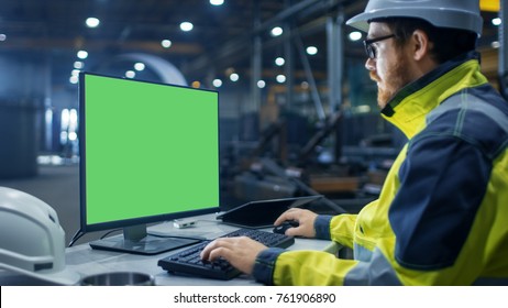 Inside The Heavy Industry Factory Industrial Engineer Works On The Personal Computer With Green Mock-up Screen.