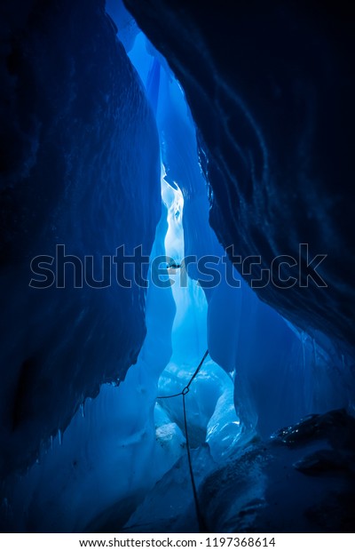 Inside a huge moulin or crevasse tunnel, nearly\
30 meters under the surface of the glacier, looking back toward the\
entrance. A rope secured by ice screws and carabiners leads the way\
out to safety.