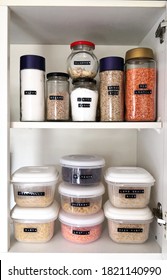 The Inside Of A Kitchen Cupboard Containing  Dry Food Organised In Transparent, Labeled Jars And Plastic Containers.  Organised Pantry And Kitchen Concept.