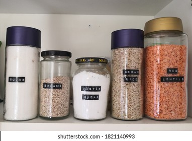 The Inside Of A Kitchen Cupboard Containing  Dry Food Organised In Transparent, Labeled Jars .  Organised Pantry And Kitchen Concept.