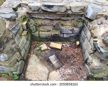 The Inside Of A Large Stone Fire Place Next To The River That's Falling Apart. The Bricks Are Breaking Off And Falling To The Ground. The River Makes For A Scenic View In The Park.