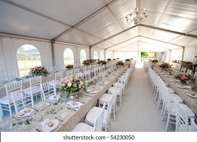 The inside of a massive white wedding tent with tables and chairs already in position