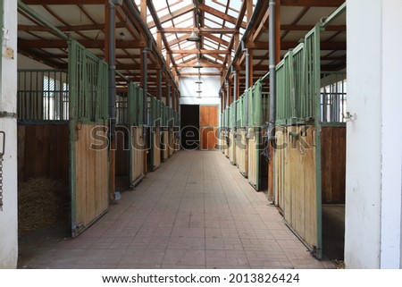 Inside modern clear stable or barn with horse boxes. Passageway view in natural light in the end. Cleared empty stall in the stable keeping sport horses