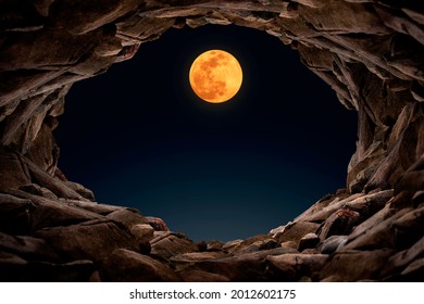 Inside a mysterious cave at night Looking out to see a full moon, a cave filled with rocks.