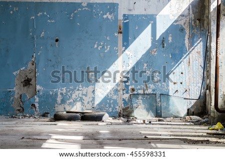 Inside An Old Abandoned Industrial Building, Factory. The Wall With Peeling Blue Paint. Used Tires, Wheels. Many Different Garbage. Broken Glass Unit.