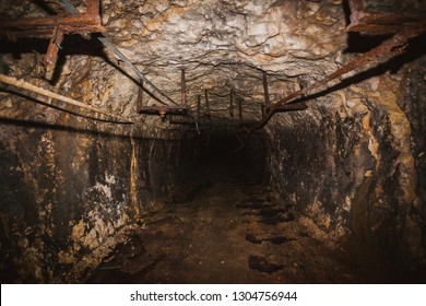 Inside old closed coal mine; dangerous tunnels full of dirt, lots of abandoned rusty equipment, devastated industrial place