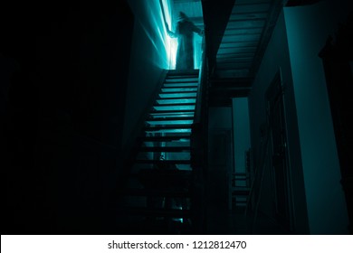 Inside of old creepy abandoned mansion. Silhouette of horror ghost standing on castle stairs to the basement. Spooky dungeon stone stairs in old castle with light. Horror Halloween concept