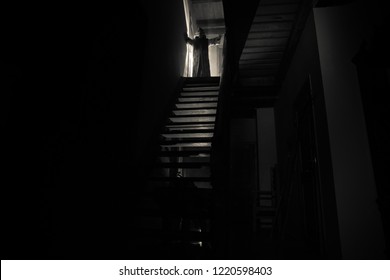 Inside Of Old Creepy Abandoned Mansion. Silhouette Of Horror Ghost Standing On Castle Stairs To The Basement. Spooky Dungeon Stone Stairs In Old Castle With Light. Horror Halloween Concept