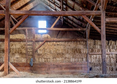 Inside Old Dirty Barn with Hay Bales Dark Wood Beams and Wooden Ladder Streaming Light from Window