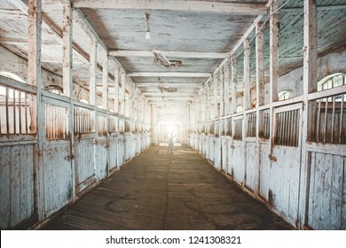 Inside old wooden stable or barn with horse boxes, tunnel or corridor view with light in the end, toned