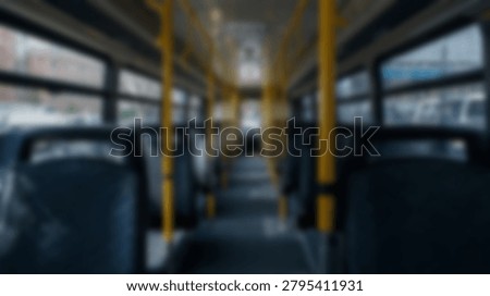 Inside a public bus, rows of seats are visible, along with vertical poles for passengers to hold. The interior is well-lit, suggesting a daytime shot. The focus is on the buss interior design and functionality.