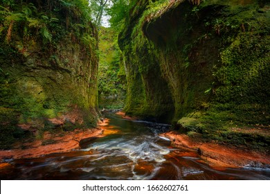 Inside of the Devil’s Pulpit gorge, with beautiful running water and red river bed with walk in the water towards a waterfall, near Glasgow, Scotland, UK - Shutterstock ID 1662602761