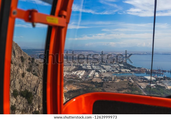 Inside of red cabin of cableway on\
picturesque mountains. Cabin driving over huge mountains. Beautiful\
view at city in distance. Horizontal color\
photography.