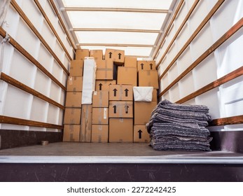 The inside of a removal van, showing fabric blankets stacked and a background of cardboard boxes. Concept for moving home, furniture protection, storage, packing and transportation. Copy space.