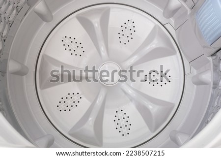 Inside of a top load washing machine showing the washing tub with filter on the side and the pulsator installed on the bottom. Interior details of a clothes washer inner drum. Closeup top view.