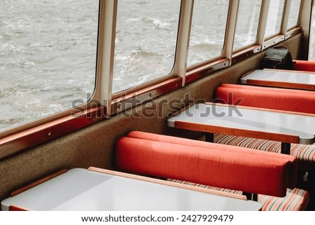 Inside tourism Milford Sound cruise ferry boat with cushioned red and striped seats grey tables and windows to view scenic water views at leisure