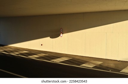 Inside of an underpass with concrete wall with two road sign, divided in two by the shadow of the bridge. Two lane road in front. Background for copy space.