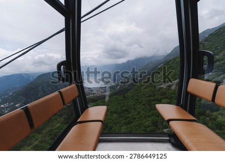 Inside view of a cable car cabin with a breathtaking panoramic outlook of mountains, sea bay, and clouds.