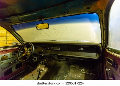 Inside view of old broken car interior with dusty vehicle dashboard, back mirror, driving steering wheel and dirty wind screen with title SALE written outside. Concept of sale pre-owned cars on the
