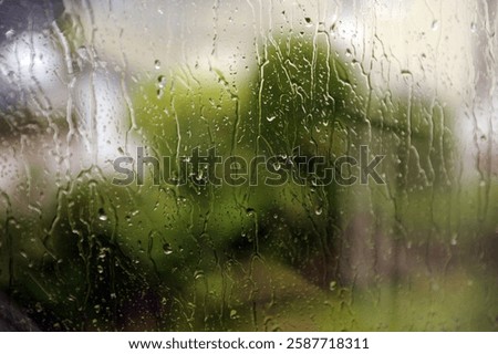 Inside view through wet window pane on rainy day. Abstract pattern of raindrops and green background.
