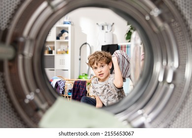 Inside The Washing Machine, A Little Boy Is Putting Colorful Clothes Into The Drum Through The Open Door, Helping Father With Household Chores.