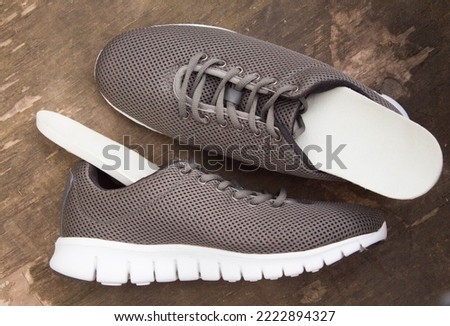 Insoles and sports shoes on old wooden board. Prevention of orthopedic foot diseases, foot care. Rustic background. Top view.