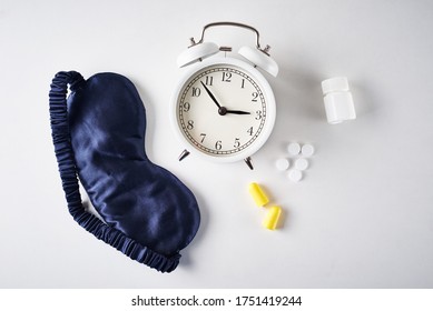 Insomnia, Depression And Sleeping Trouble Problem Concept. Alarm Clock, Sleeping Mask, Ear Plugs And Pills On White Background, Top View