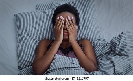 Insomnia and pain. African american girl closed eyes with hands in bed, dark - Powered by Shutterstock