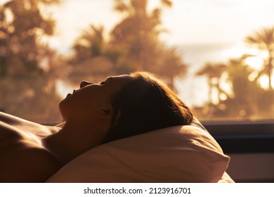 Insomnia. Silhouette of woman lying on pillow on bed and can't sleep. Bedroom with panoramic window and view on palm tree sea beach at sunset, sunrise.  - Shutterstock ID 2123916701