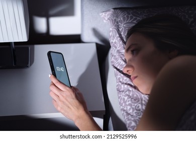 Insomnia. Sleepless woman looking the time unable to sleep at night. Sad tired person with disorder in bed. Phone clock. Bad dream and problem keeping awake. Unhappy lady trying to fall asleep.