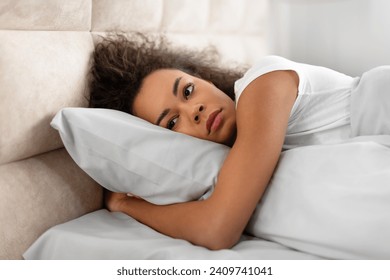 Insomnia. Unhappy black young woman lying alone awake in her domestic bedroom, feeling sad and depressed looking away, struggling with sleep issues. Mental health problems - Powered by Shutterstock