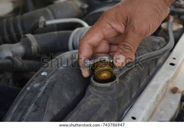 Inspect the car radiator, the\
hands of a mechanic who works in a car repair shop, a rusty\
radiator cap.