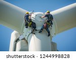 Inspection engineers preparing to rappel down a rotor blade of a wind turbine in a North German wind farm on a clear day with blue sky.