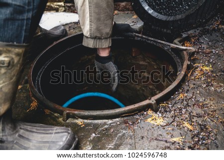 Inspection of the sewage well. The worker's hand in the working glove is lowered into the open hatch of the sewer well which is filled with water