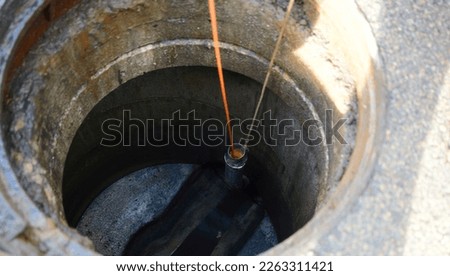 Inspection through manhole city sewage system. Opening the sewer cover in the middle of the asphalt street. Orange cable on a roll is automatically unrolled in the sewer system for inspection of water