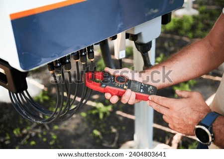 Inspector checking output voltage level of inverter. Professional worker using current clamps to know how solar panel working. Techinician service of PV battery.