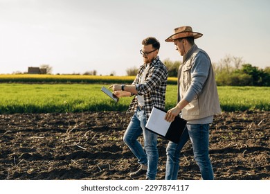 Inspector and a farmer walk across the farmland. The inspector points to a tablet he is holding. - Shutterstock ID 2297874117