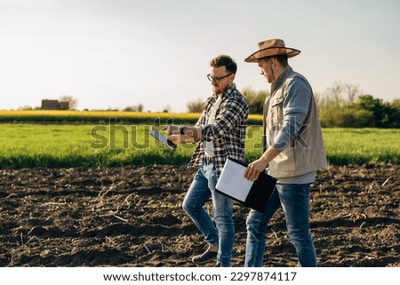 Inspector and a farmer walk across the farmland. The inspector points to a tablet he is holding.
