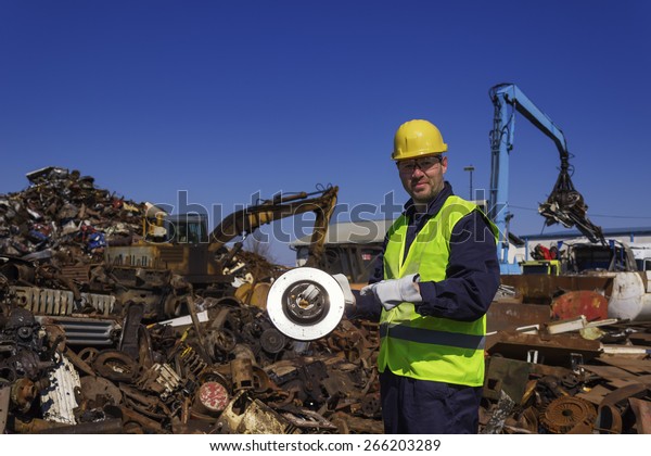 Inspector hold old car rotor on\
junkyard. Two cranes in background. Copy space\
available.