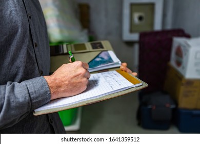 Inspector Holding A Notebook In His Hand During A Home Inspection In The Basement, Close Up And Selective Focus Of A Man Taking Professional Notes.