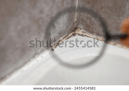 Inspector using a magnifying glass while inspecting poor-quality sealant in a bathroom covered in black mold, close-up. Mold in bathroom, problem of excessive dampness and humidity, health hazard.