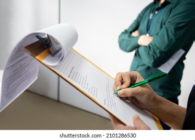 Inspector writting on a clipboard. Man in the background with arms crossed. Inspection by supervisors in a office - Shutterstock ID 2101286530