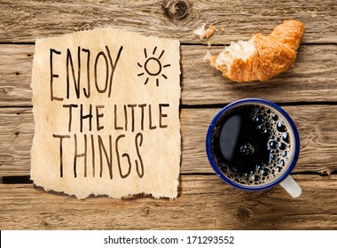 Inspirational early morning breakfast of a half eaten fresh croissant with filter coffee and a handwritten note - Enjoy the little things - reminding us to appreciate even the simple moments in life