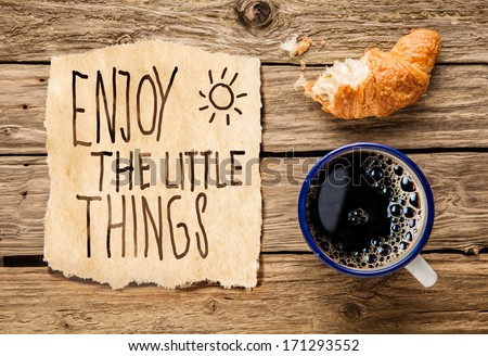 Inspirational early morning breakfast of a half eaten fresh croissant with filter coffee and a handwritten note - Enjoy the little things - reminding us to appreciate even the simple moments in life
