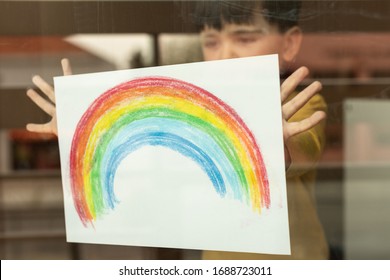 Inspirational little kid holding a drawing of a rainbow through the window 