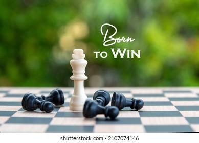 Inspirational motivational quote - Born to win. With king and black pawn chess pieces on a chessboard and green bokeh light background. Life purpose and confidence concept.