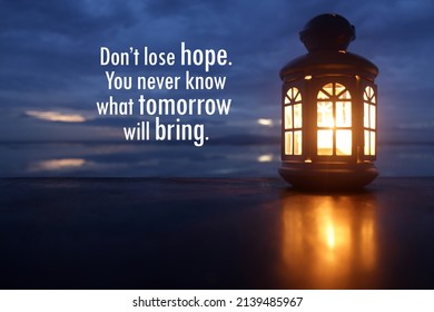 Inspirational Motivational Quote - Don't Lose Hope. You Never Know What Tomorrow Will Bring. With Lantern And Candle Light Inside On Blue Sky Over Sea Horizon Background At Dusk. Hope Concept.