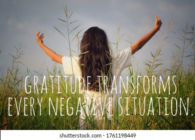 Inspirational motivational quote - Gratitude transforms every negative situation. With young woman in the field, standing alone with raised hands and open arms against the gloomy blue sky background.
