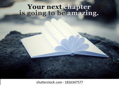 Inspirational motivational quote - Your next chapter is going to be amazing. With open book page and white paper pages flower shape decoration on a sea rock outdoor. White bokeh light background.